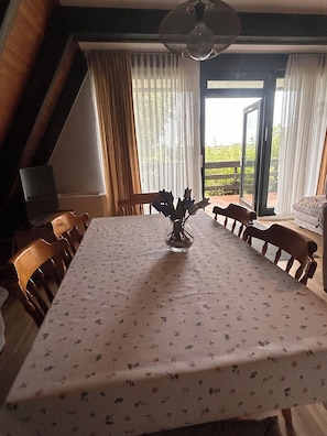 A dining area with a table set for six, a vase with flowers, wooden chairs, a ceiling fan, and a view through a glass door.
