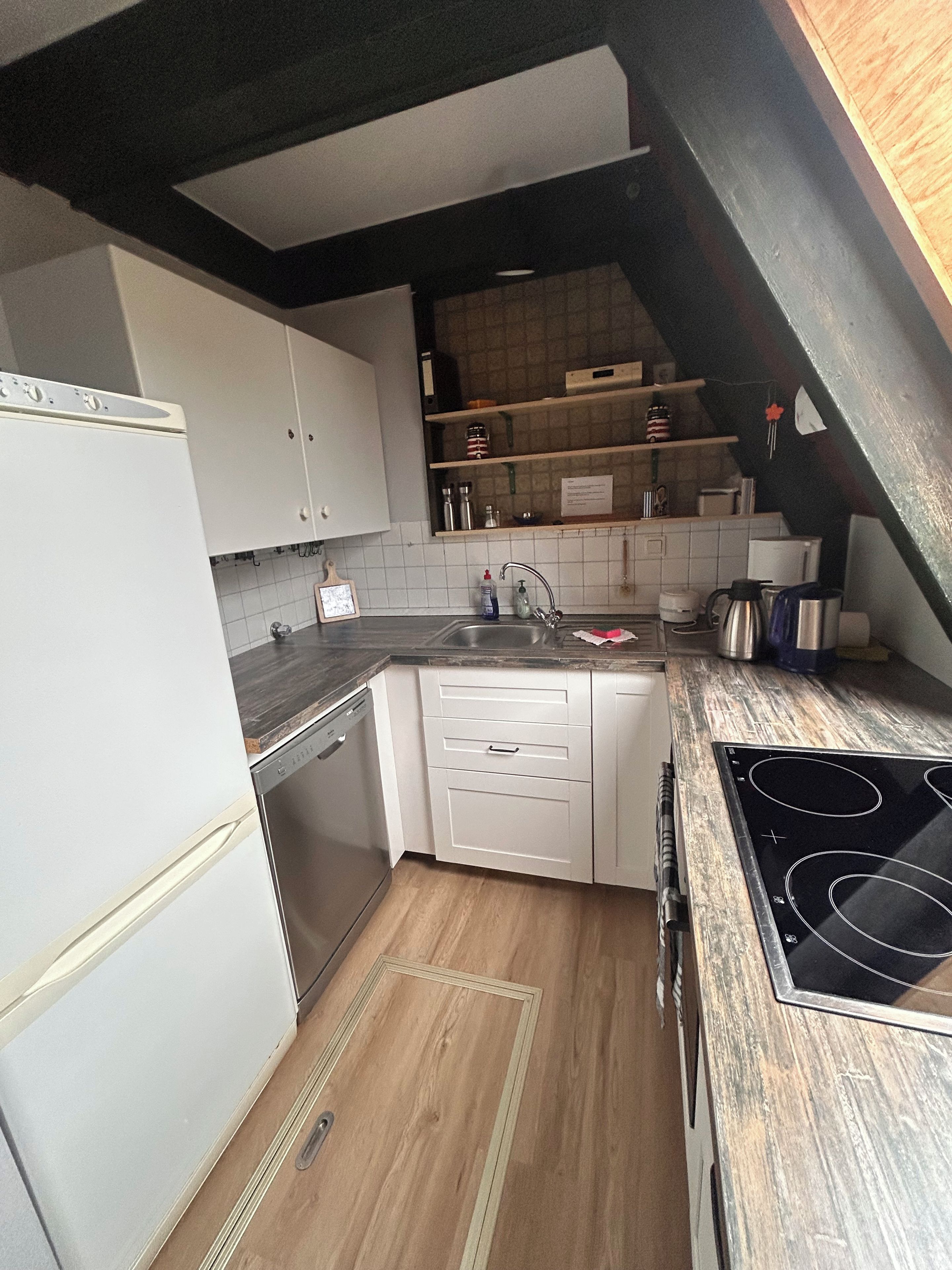 A compact kitchen with white cabinets, a built-in dishwasher, a stove, and a wooden countertop.