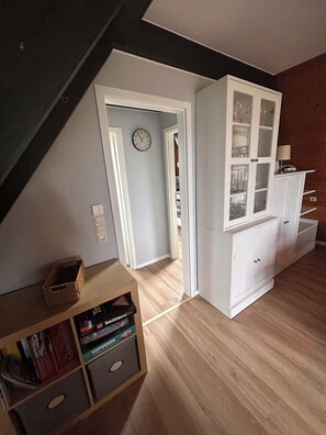 A room with a sloped ceiling, a white cabinet with glass doors, and a wooden floor.
