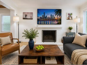 A living room with a fireplace, a sofa, a coffee table with apples, and a cityscape painting above the fireplace. - Sunset Paradaise in Fort Lauderdale (Fort Lauderdale)