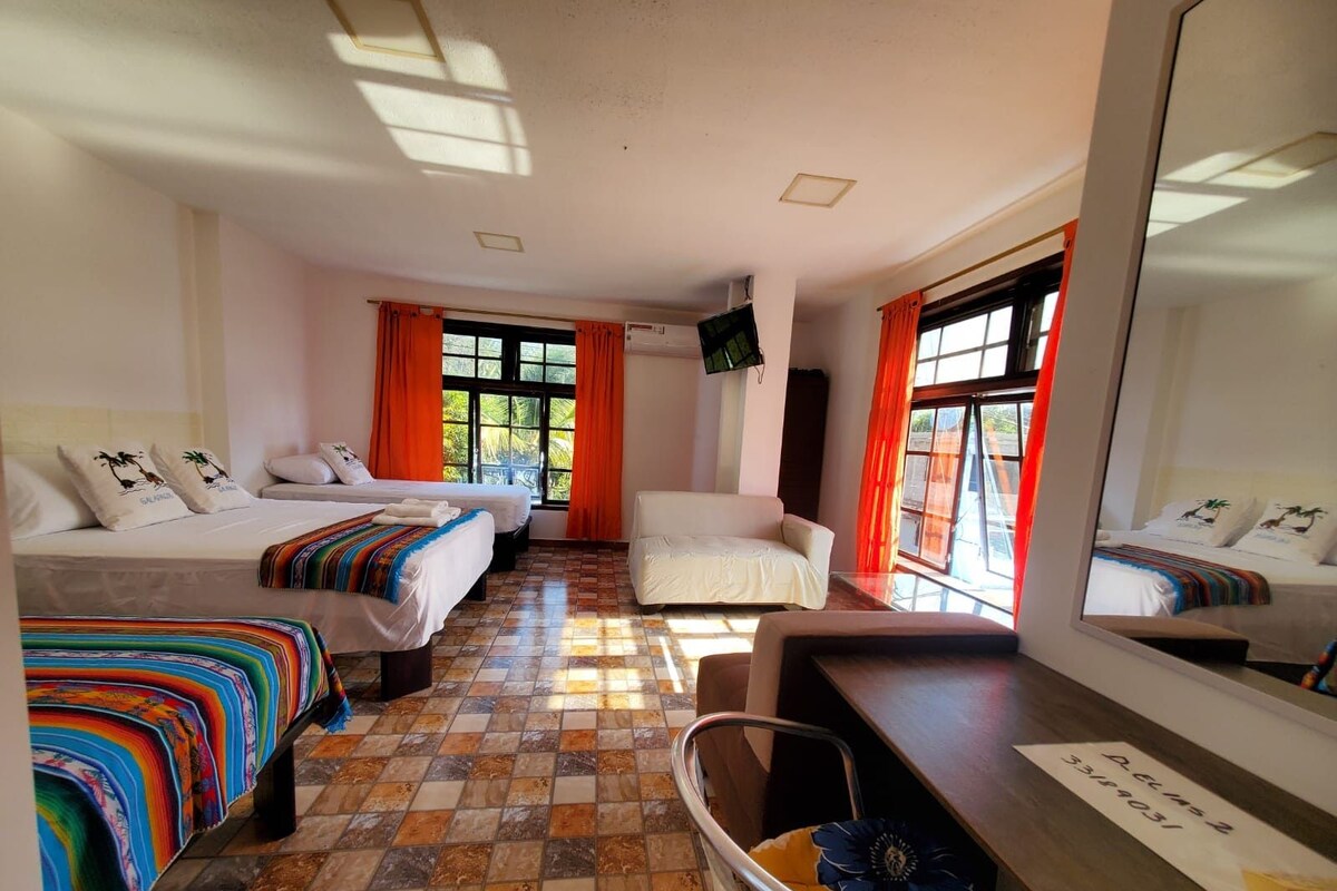 A hotel room with two beds, a sofa, a chair, a desk, and a large mirror.
