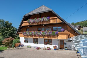 Ein zweistöckiges Gebäude mit geneigtem Dach, hölzernen Balkonen mit Blumenkästen und einem Schild, das auf ein Restaurant hinweist.