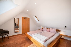 Une chambre avec un plafond en pente, un lit en bois, une table de chevet, une chaise et un miroir.