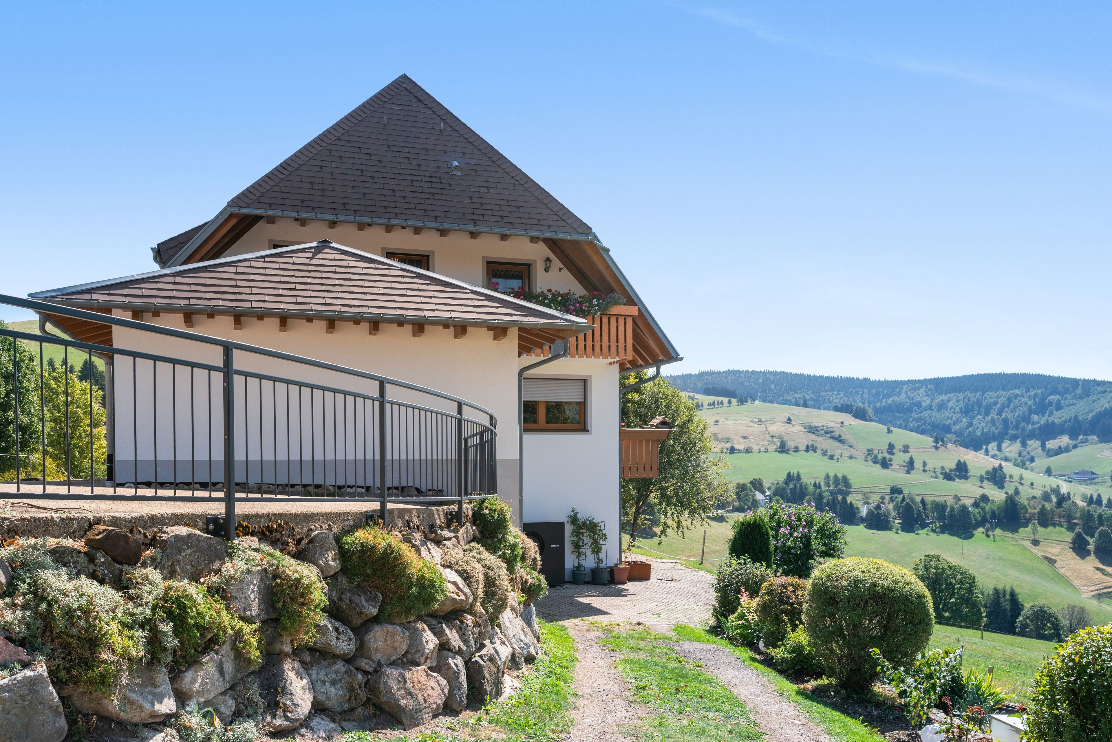 A two-story house with a balcony, a stone wall, and a view of the countryside.