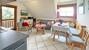 Uma sala de estar aconchegante com área de jantar, televisão na parede e janela com cortinas.