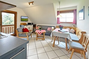 Ein gemütliches Wohnzimmer mit Essbereich, einem an der Wand befestigten Fernseher und einem Fenster mit Vorhängen.
