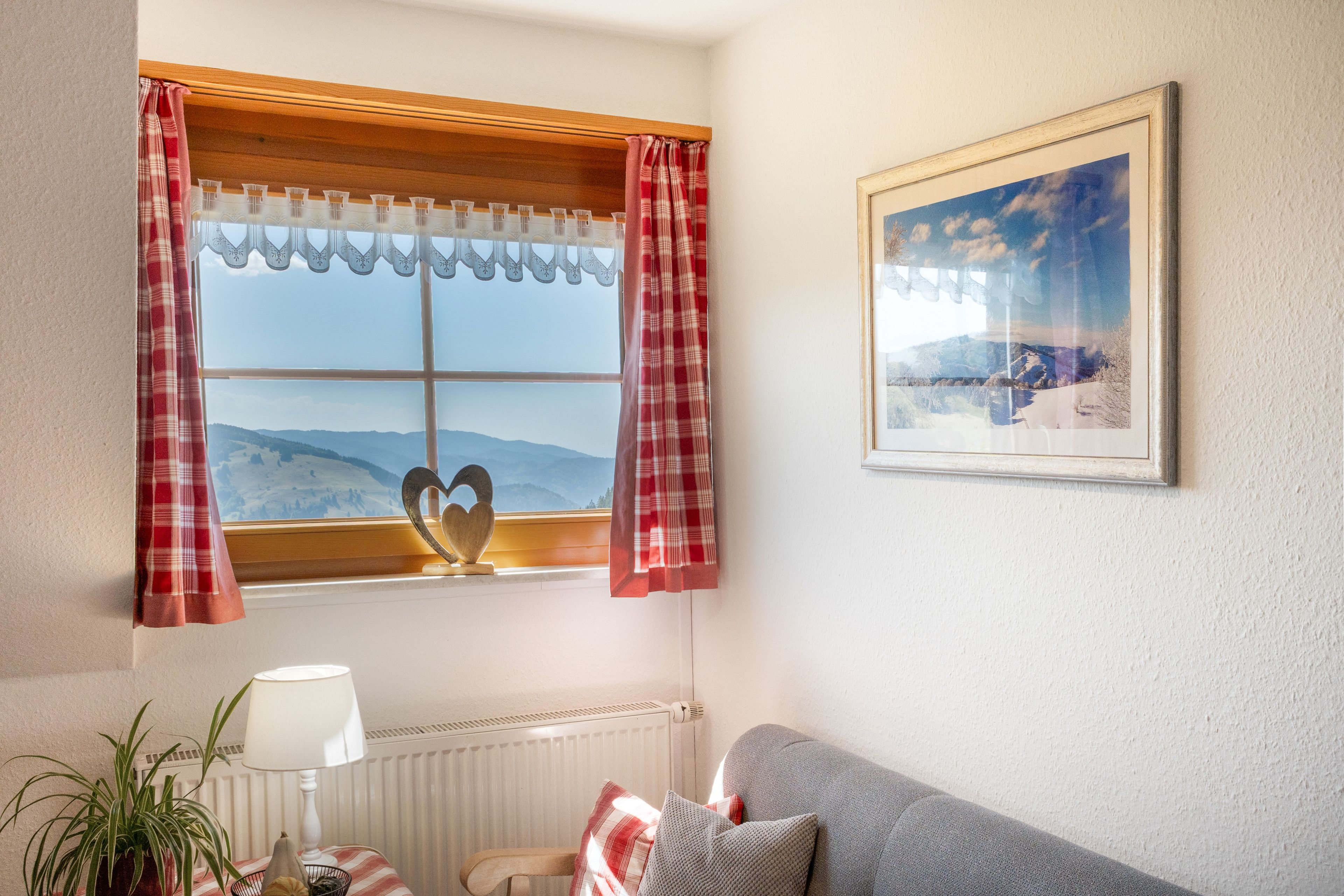 A room with a window, a framed picture, a lamp, a plant, and a sofa.