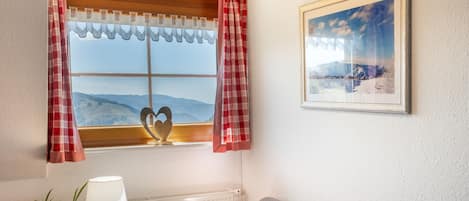 Una habitación con ventana, un cuadro enmarcado, una lámpara, una planta y un sofá.