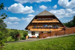 Eine zweistöckige Holzchalet mit geneigtem Dach, einem Holzbalkon mit Blumenkästen und einer weißen Außenwand.