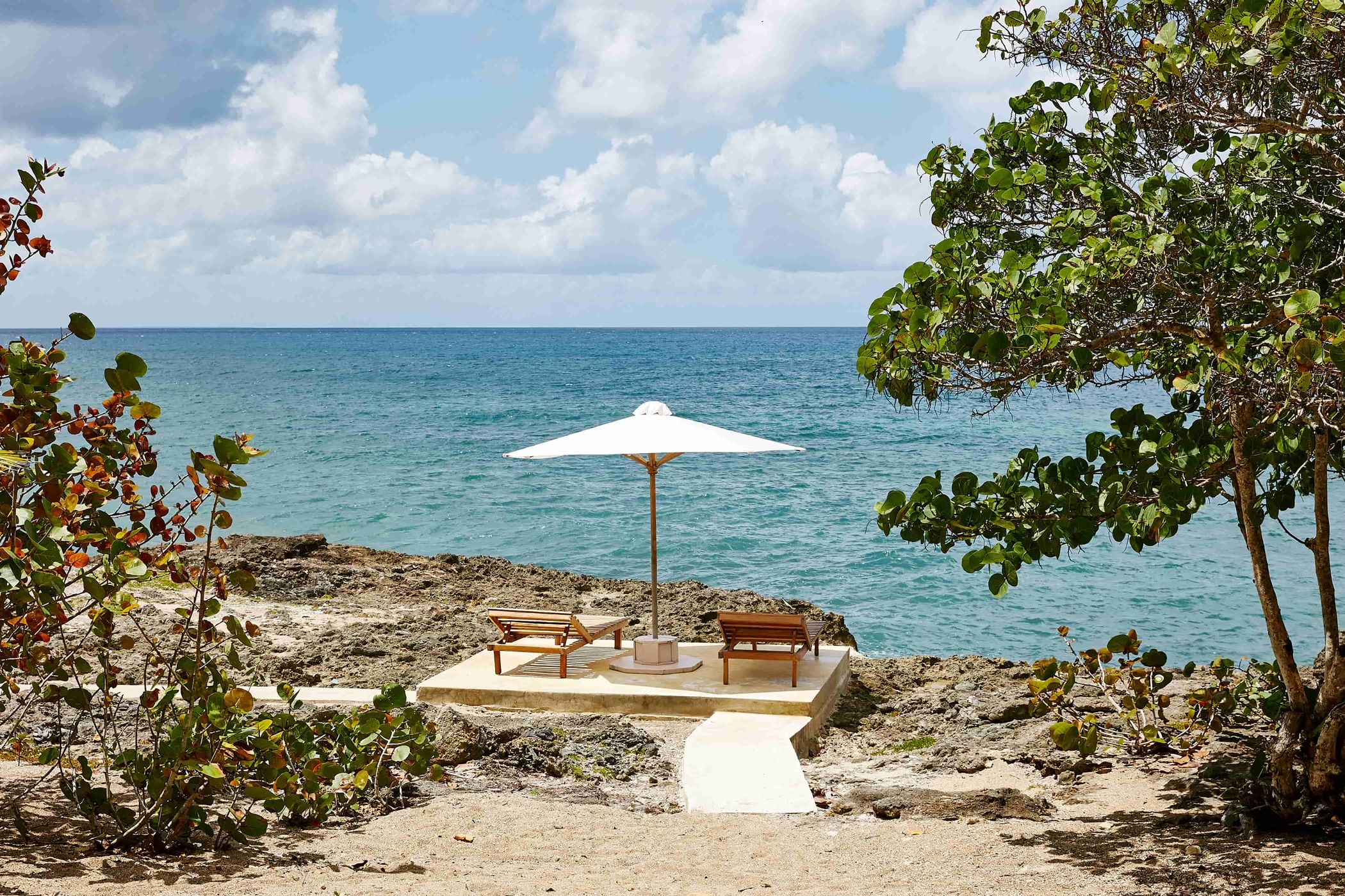A beachside seating area with two wooden benches and a white umbrella, overlooking the sea.