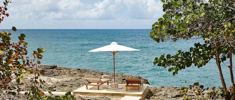 A beachside seating area with two wooden benches and a white umbrella, overlooking the sea.