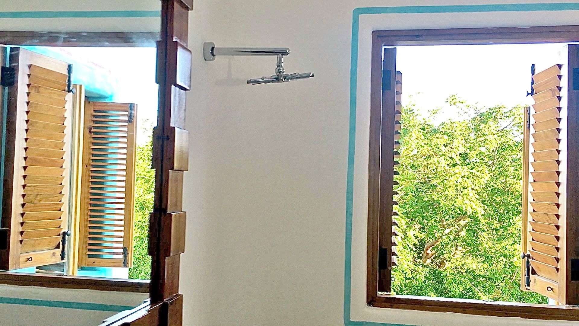 Una habitación con dos ventanas, una con contraventanas y otra con vista a follaje.