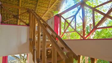 A wooden staircase leading to a thatched roof structure with a view of greenery outside.