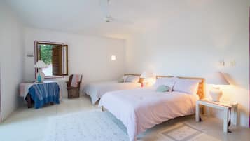 A bedroom with two single beds, a bedside table with a lamp, a small table with a lamp, a chair, and a window with shutters.