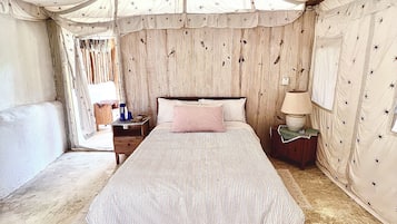 A tented room with a bed, a nightstand, a lamp, and a small table with books and a bowl.