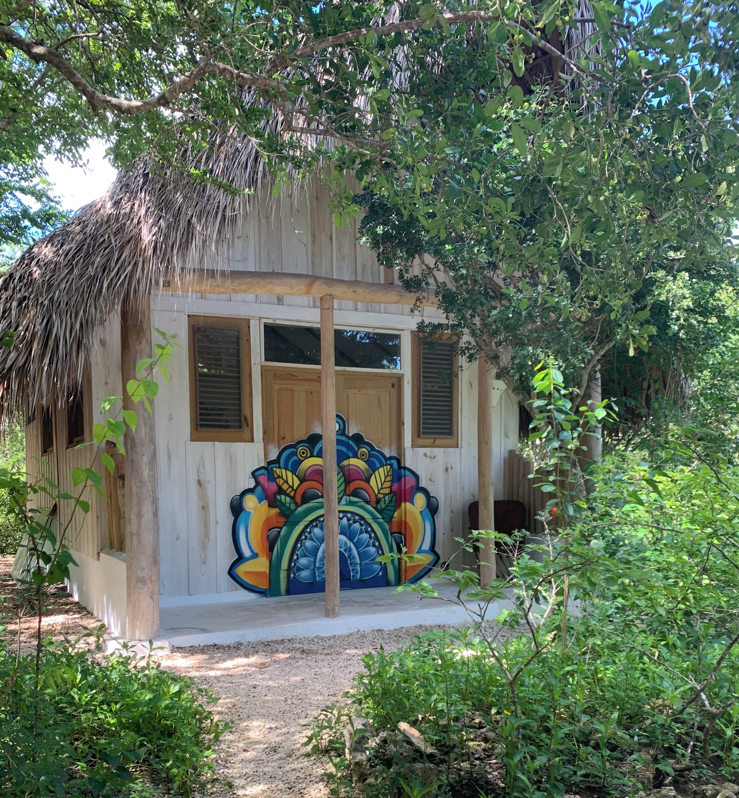 A rustic building with a colorful mural on the front wall, surrounded by greenery.