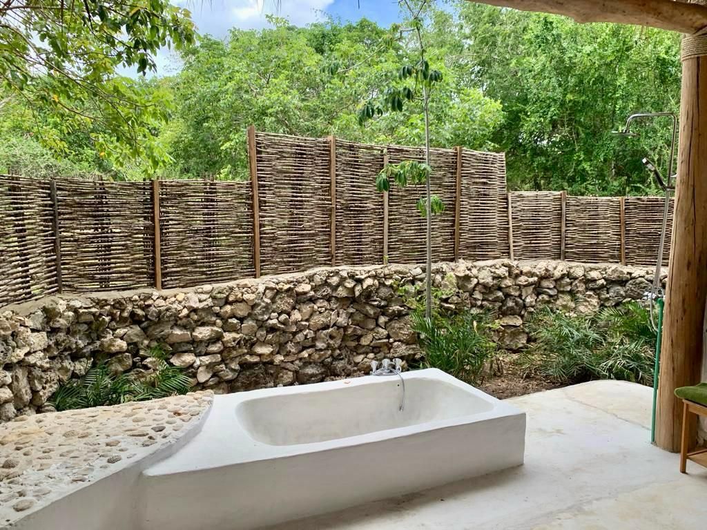 A concrete bathtub in a garden setting with a stone wall and a bamboo fence.