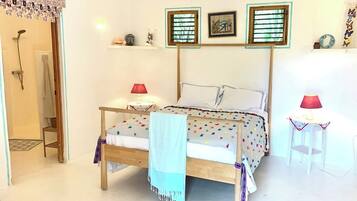 A bedroom with a wooden bed, two bedside tables with lamps, a ceiling fan, and a shower area.