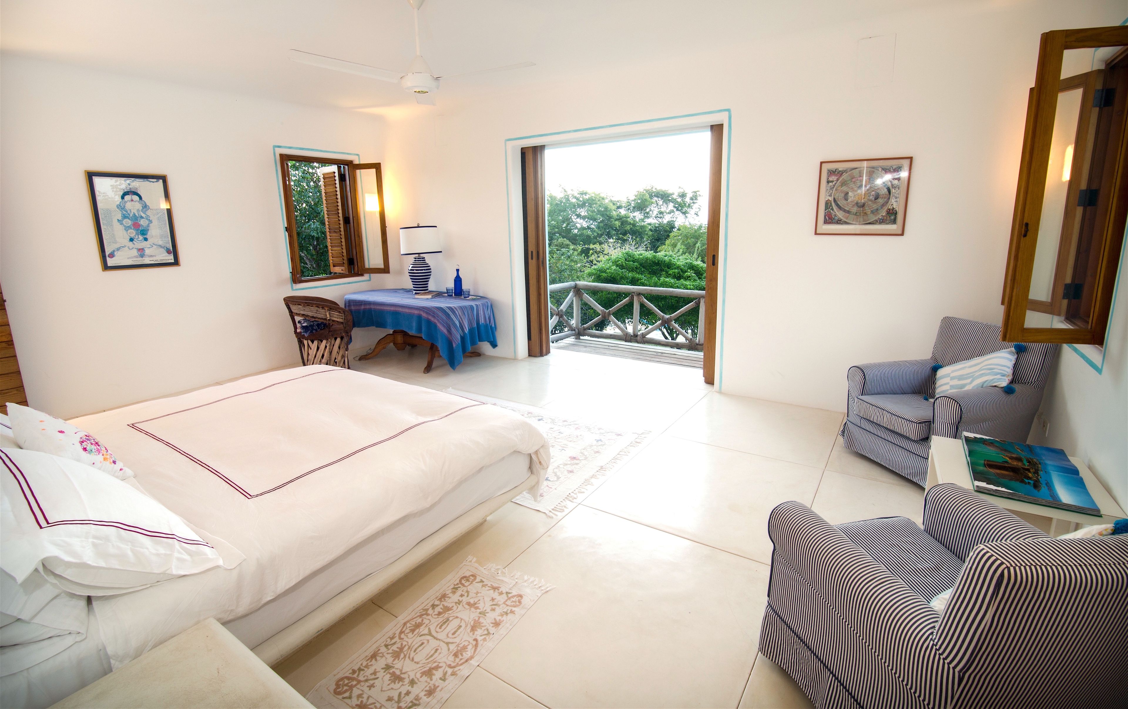 A bedroom with a bed, a chair, a table, and a balcony with a railing.
