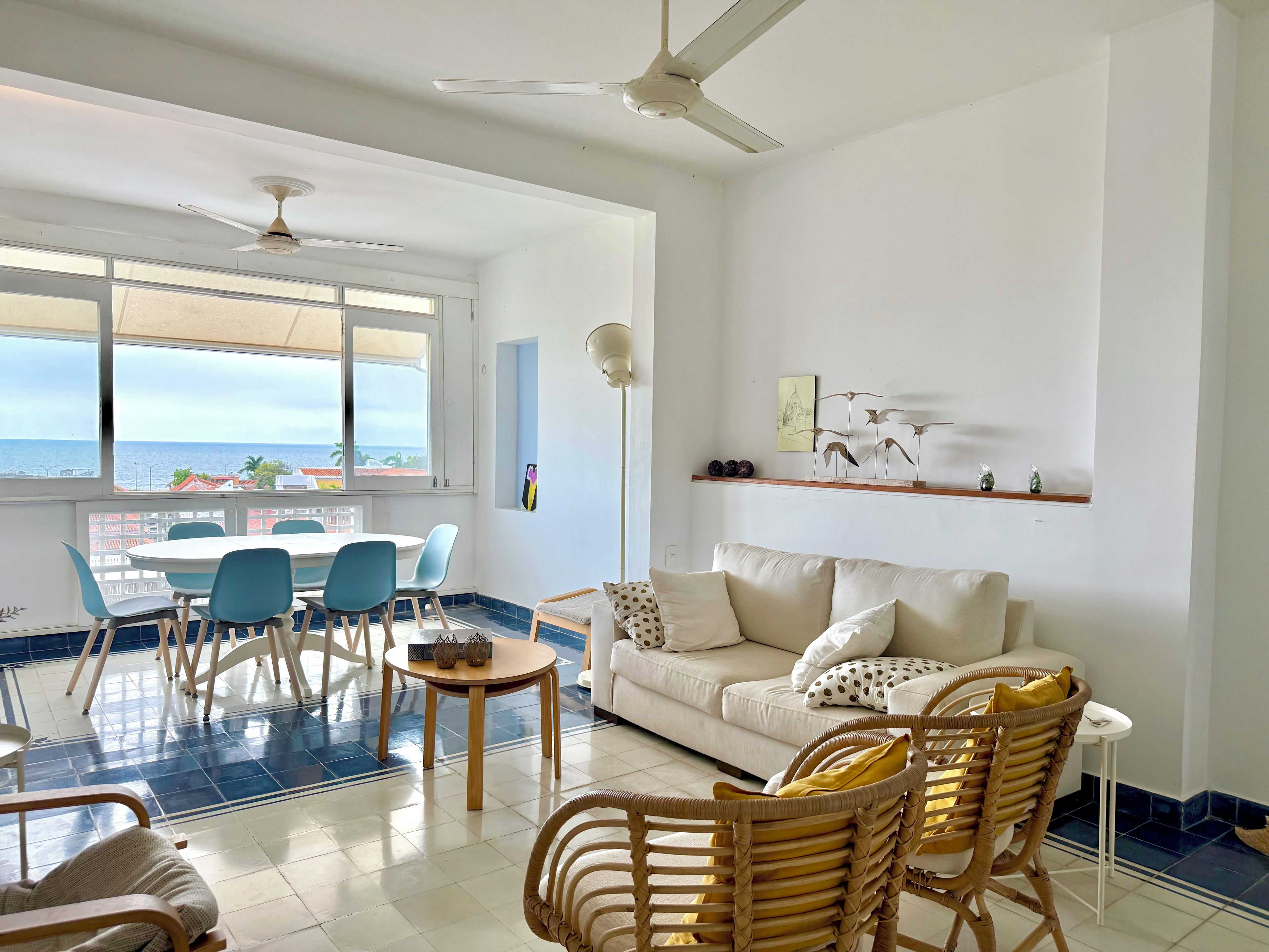 A living room with a white sofa, blue chairs, a round table, and a ceiling fan.