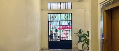A hotel lobby with a check-in counter, a tiled floor, a large window with bars, and a potted plant.