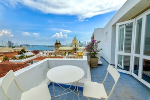 Ein Balkon mit weißem Tisch und Stühlen, der auf eine Stadtansicht mit einer markanten Kirche und einem Gewässer blickt.