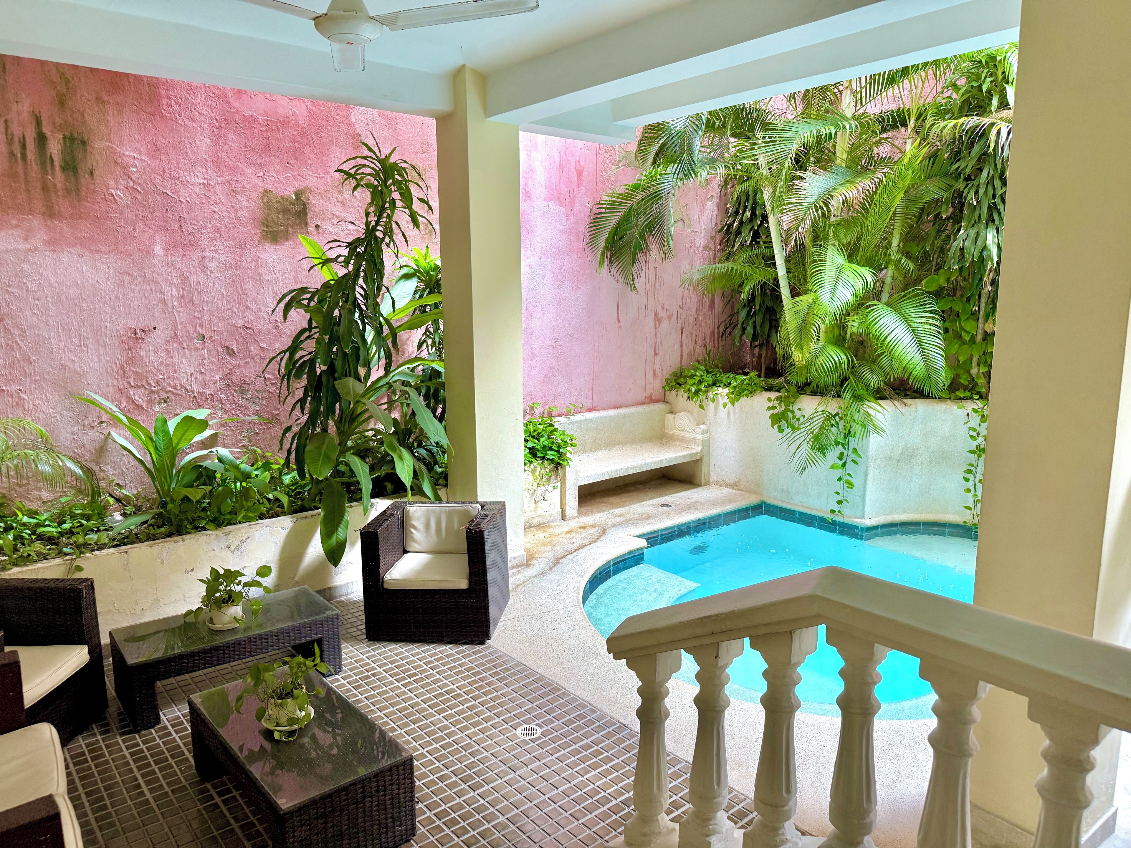 A poolside area with wicker furniture, a white bench, and lush greenery.