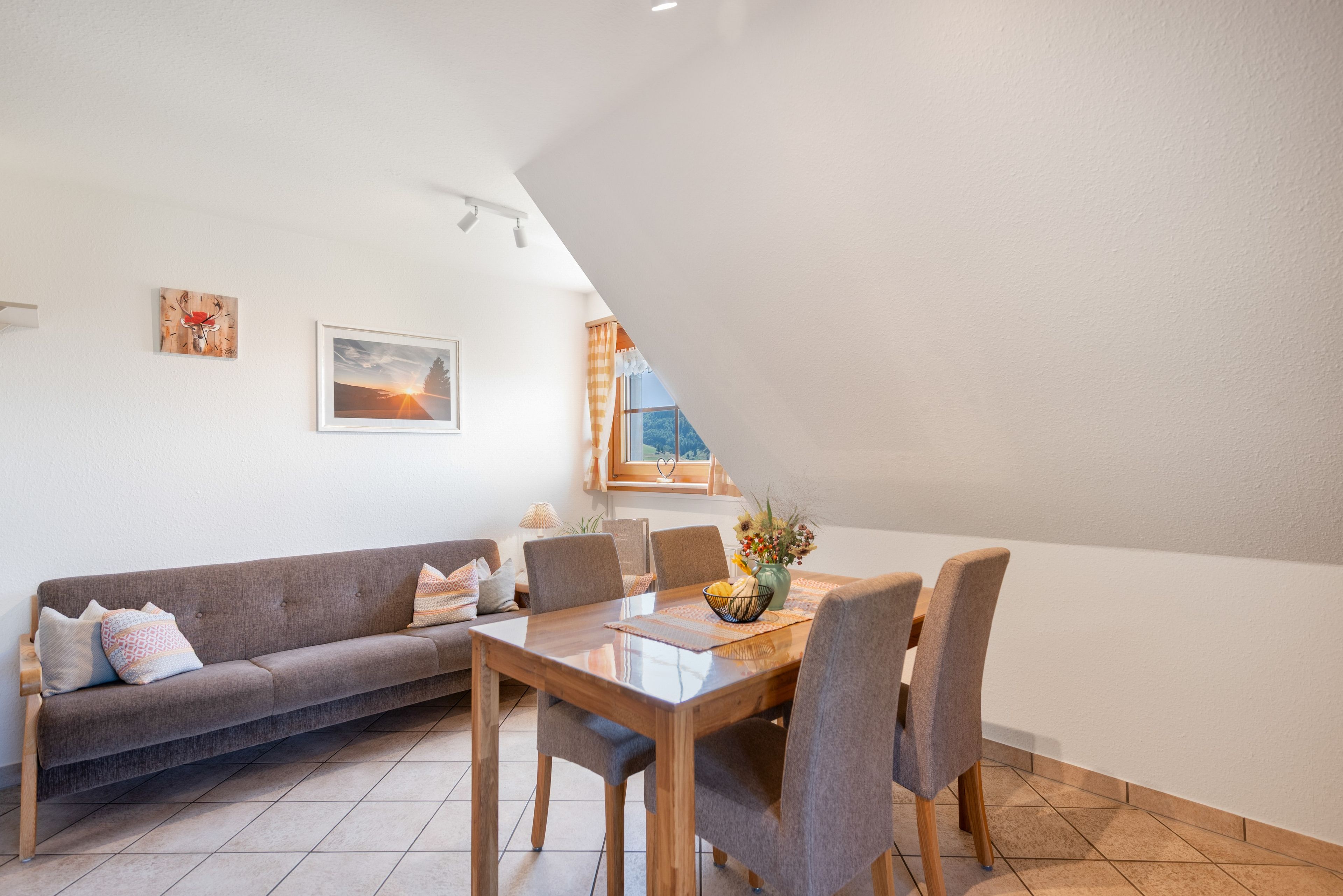 A dining area with a wooden table and chairs, a sofa, and a window with curtains.