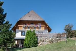 A two-story chalet with a wooden balcony, a stone wall, and a fenced yard. - Apartment 'Ferienwohnung Waldzauber' with Mountain View, Shared Terrace and Wi-Fi (Münstertal/Schwarzwald)