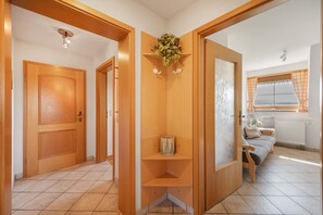 A hallway with wooden doors, a shelf with a plant, and a view of a living area with a sofa and window. - Apartment 'Ferienwohnung Waldzauber' with Mountain View, Shared Terrace and Wi-Fi (Münstertal/Schwarzwald)
