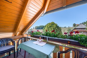 A wooden balcony with a table set for two, overlooking a garden with flowers and a view of a village. - Apartment 'Ferienwohnung Waldzauber' with Mountain View, Shared Terrace and Wi-Fi (Münstertal/Schwarzwald)