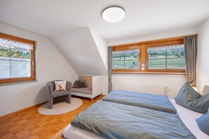 A bedroom with a sloped ceiling, a bed, a chair, a window with curtains, and a view of a green landscape. - Apartment 'Ferienwohnung Waldzauber' with Mountain View, Shared Terrace and Wi-Fi (Münstertal/Schwarzwald)