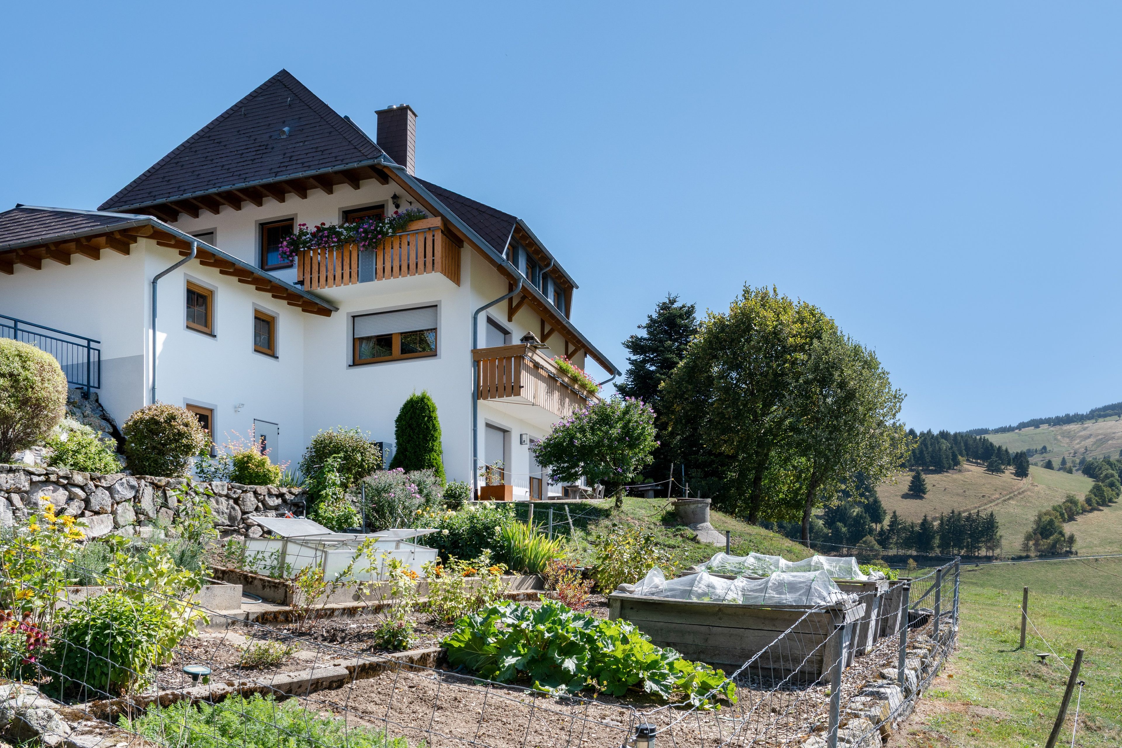 A two-story house with a sloped roof, wooden balconies, and a stone wall.