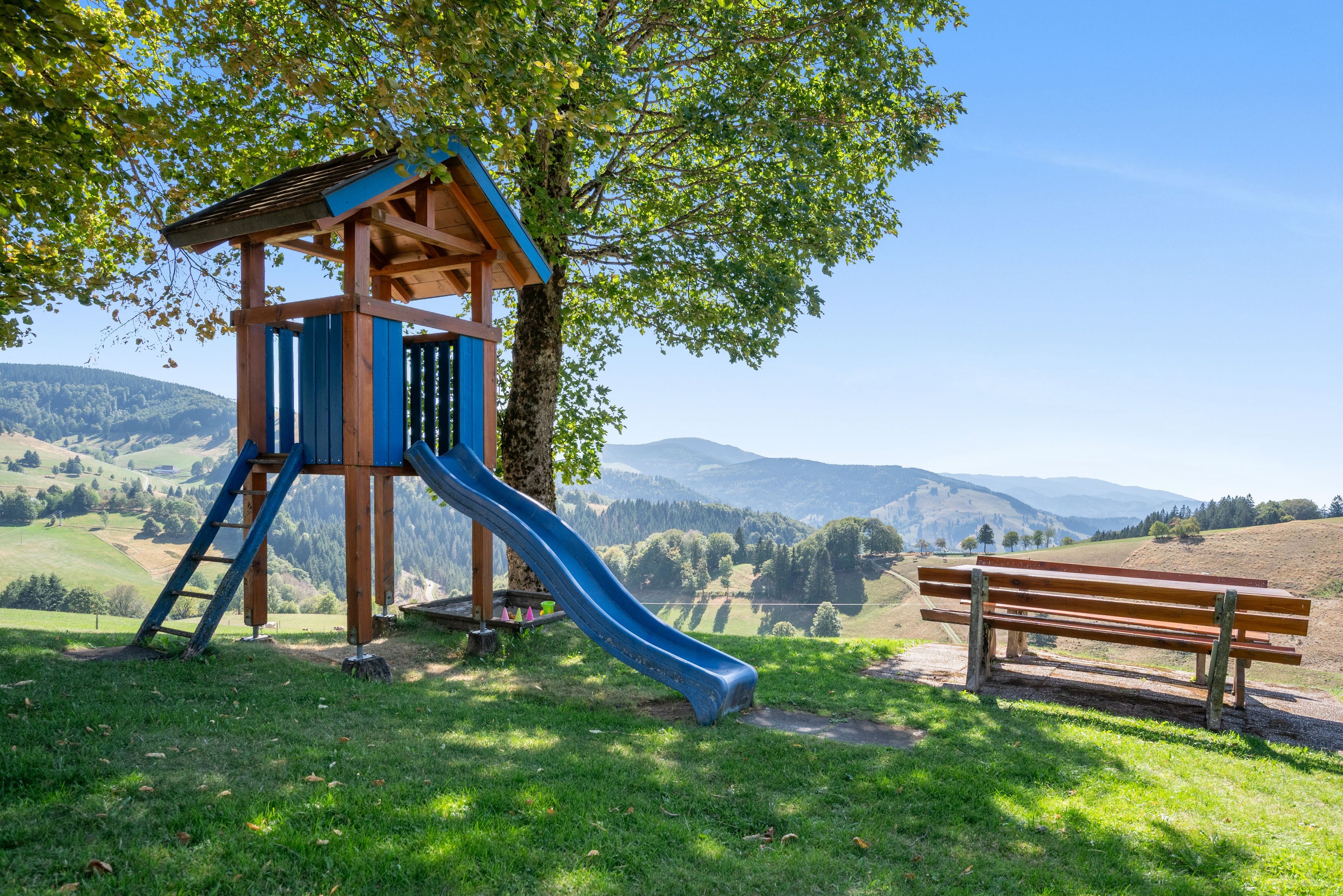 A playground with a slide and a wooden bench in a park with a mountain view.