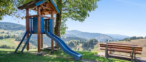 Un parque infantil con un tobogán y un banco de madera, con vista a la montaña.