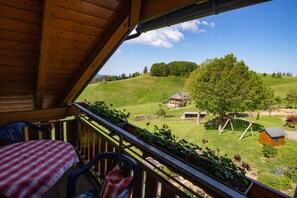 Ein Holzbalkon mit Blick auf eine ländliche Landschaft, darunter ein Haus und ein Baum.