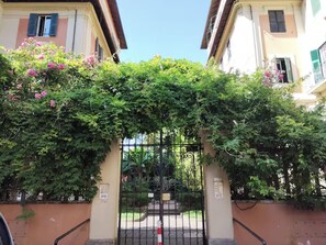 A gated entrance with a metal gate, surrounded by lush greenery and flowering plants. - La Dimora Torlonia Elegance & Light in Rome (Roma)
