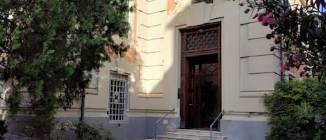 A building with a large wooden door, a small window with a metal grille, and a set of stairs leading to the entrance.