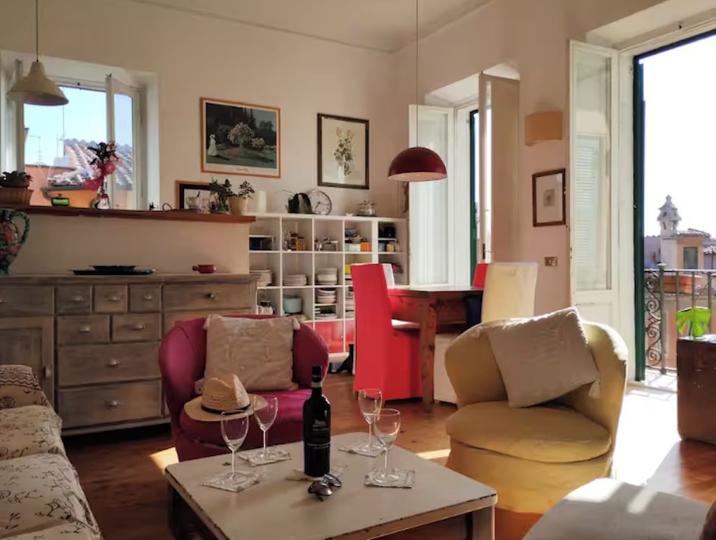 Una sala acogedora con un sofá, una mesa de comedor con copas de vino, una silla roja y una estantería.