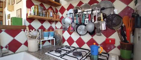 A kitchen with a gas stove, a sink, and various kitchen utensils and cookware.