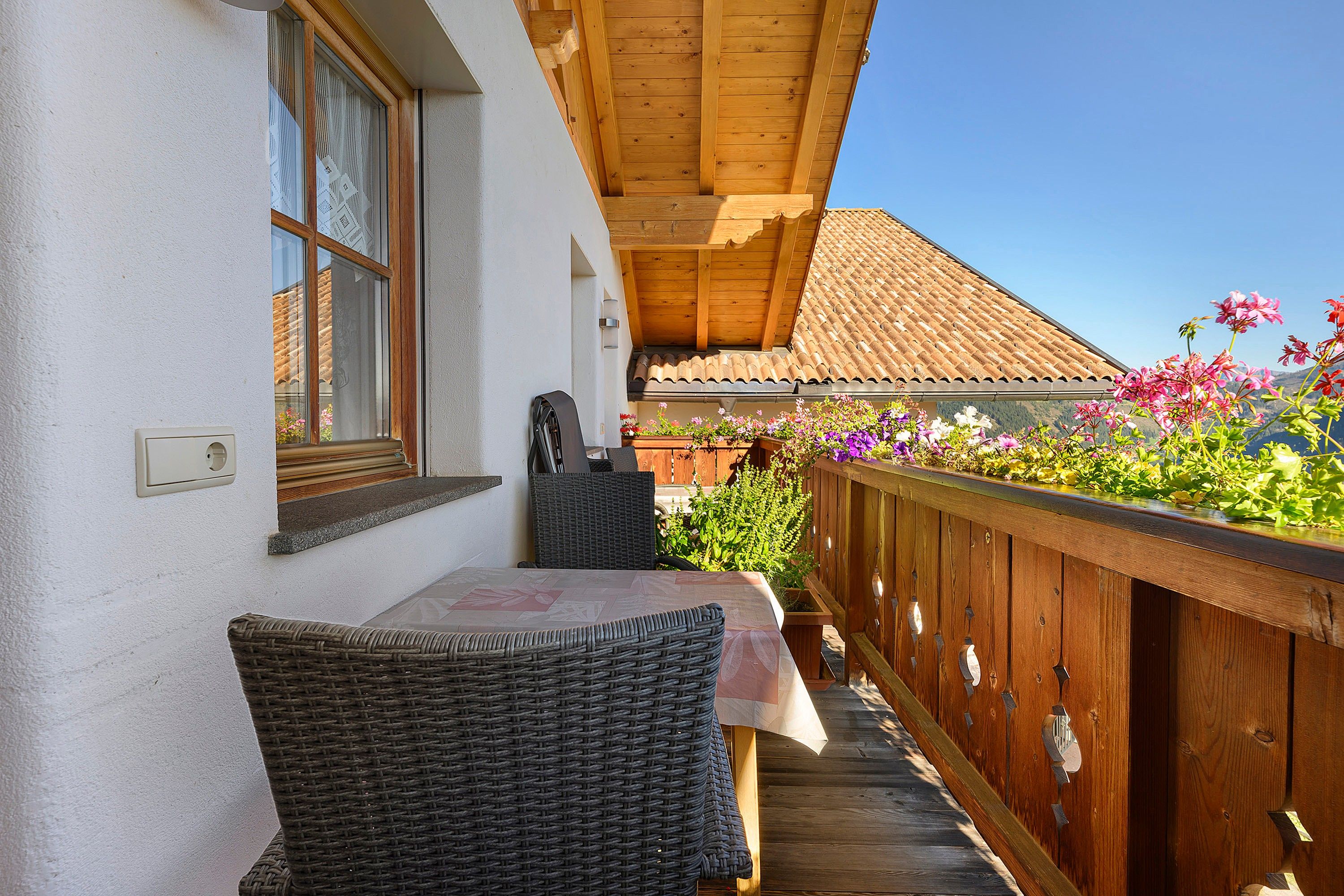 A balcony with wicker furniture, a wooden railing, and potted plants.
