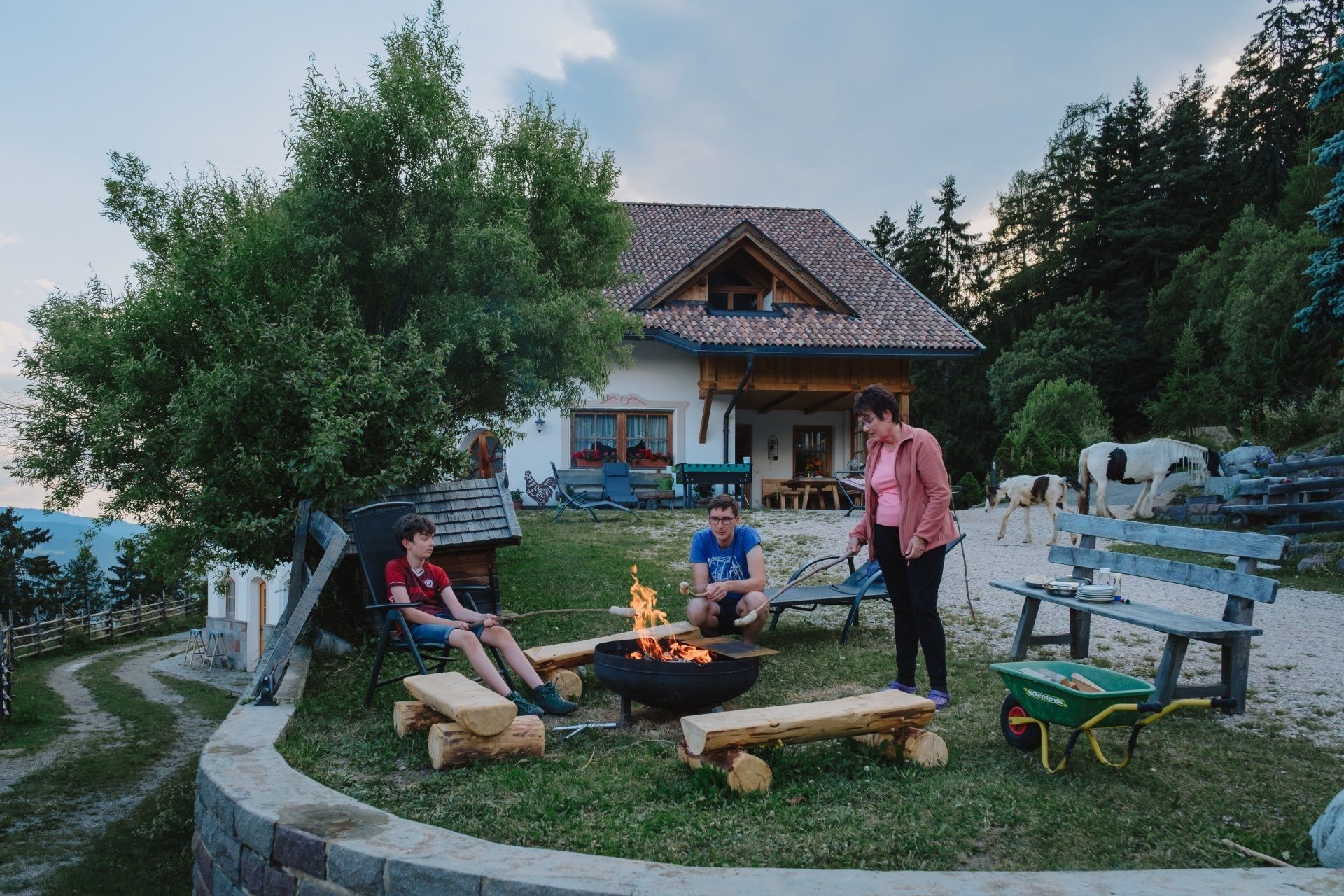 A rustic outdoor setting with a house, a fire pit, and a wooden bench.
