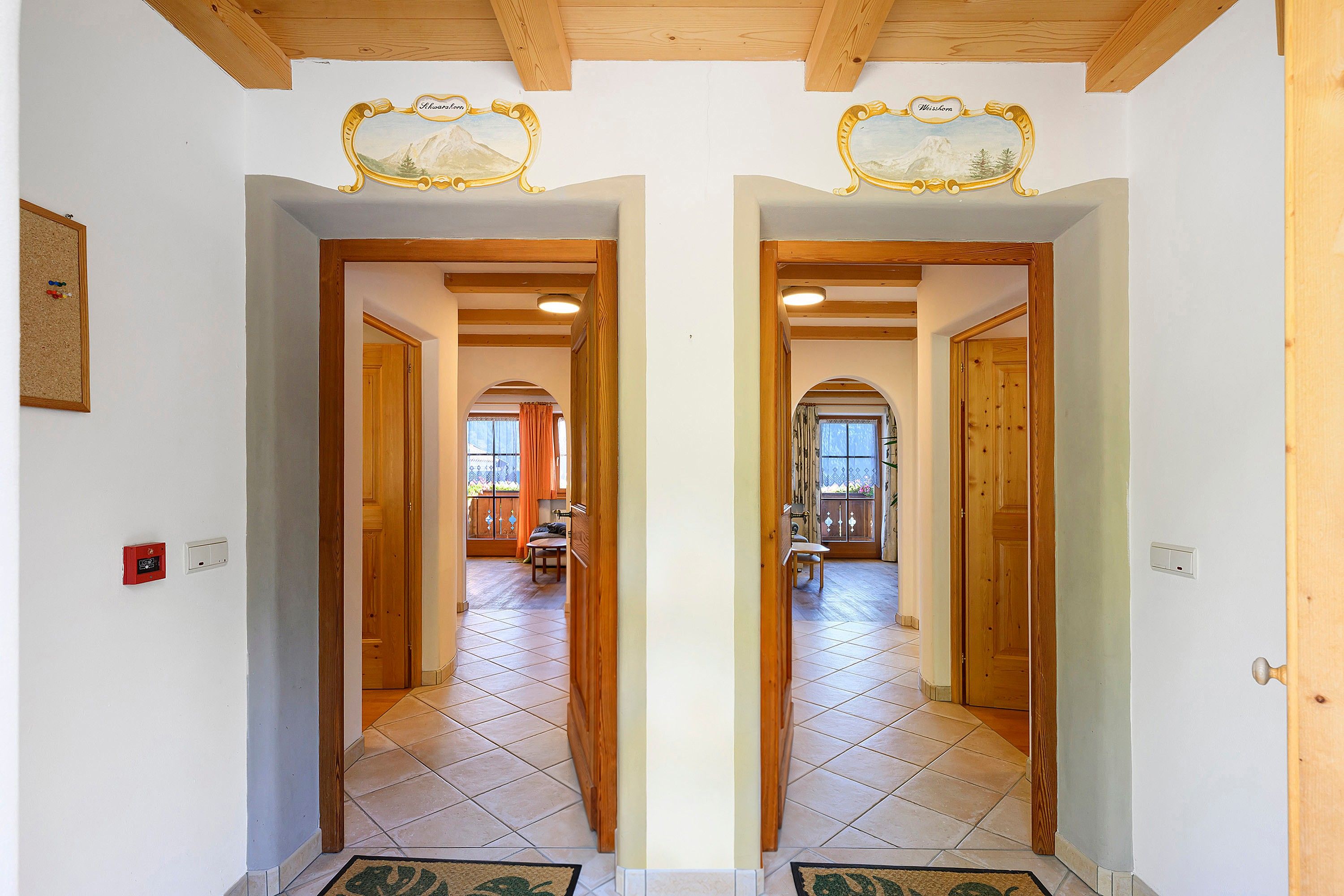 Un couloir avec un mur recouvert de miroirs, des encadrements de porte en bois et un sol carrelé.