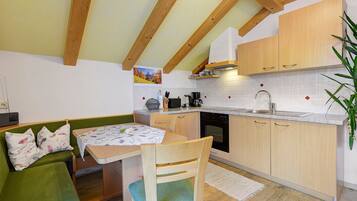 A compact kitchen with wooden cabinets, a dining table with chairs, and a built-in oven.