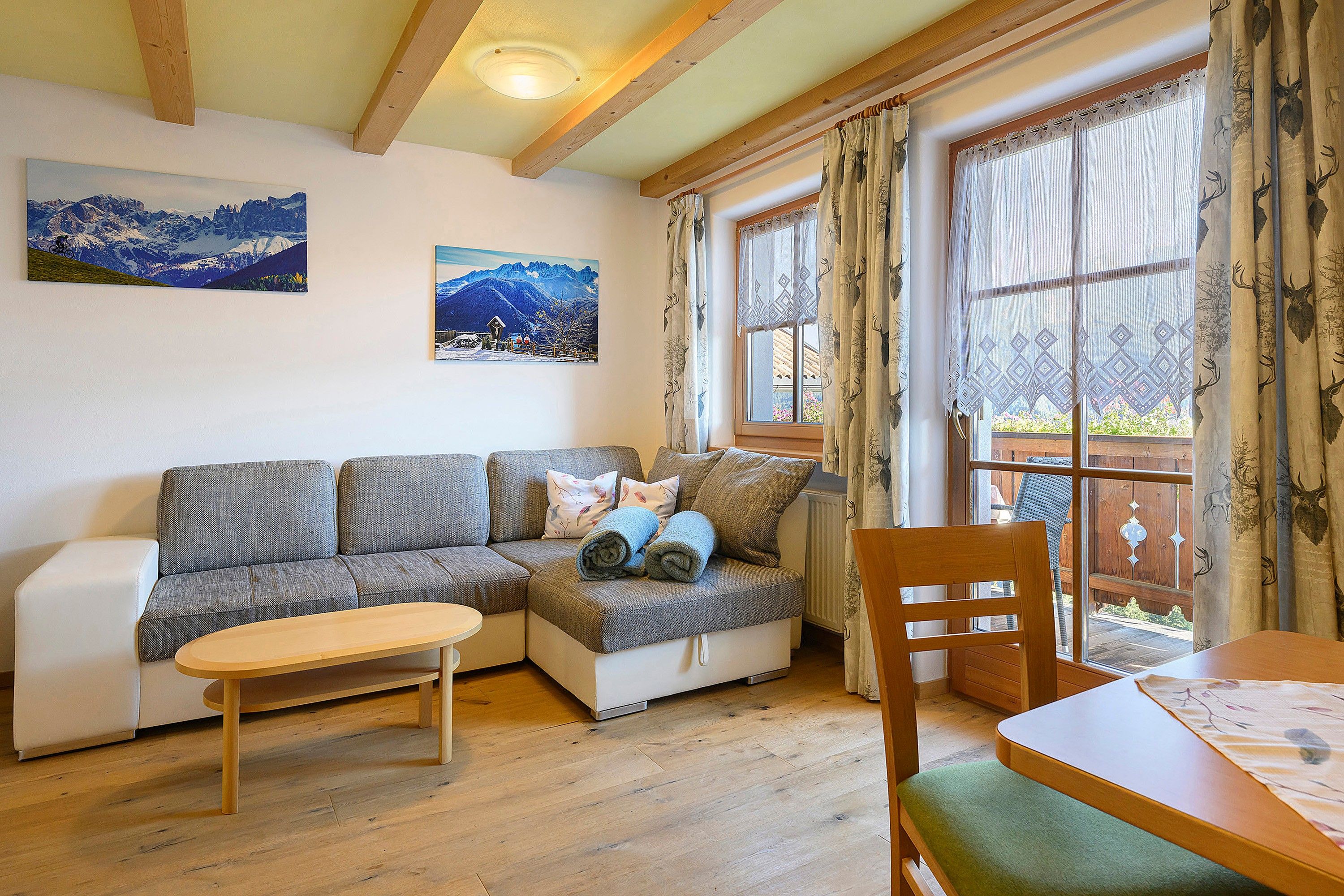 A cozy living room with a sectional sofa, a small wooden table, and a window with curtains.