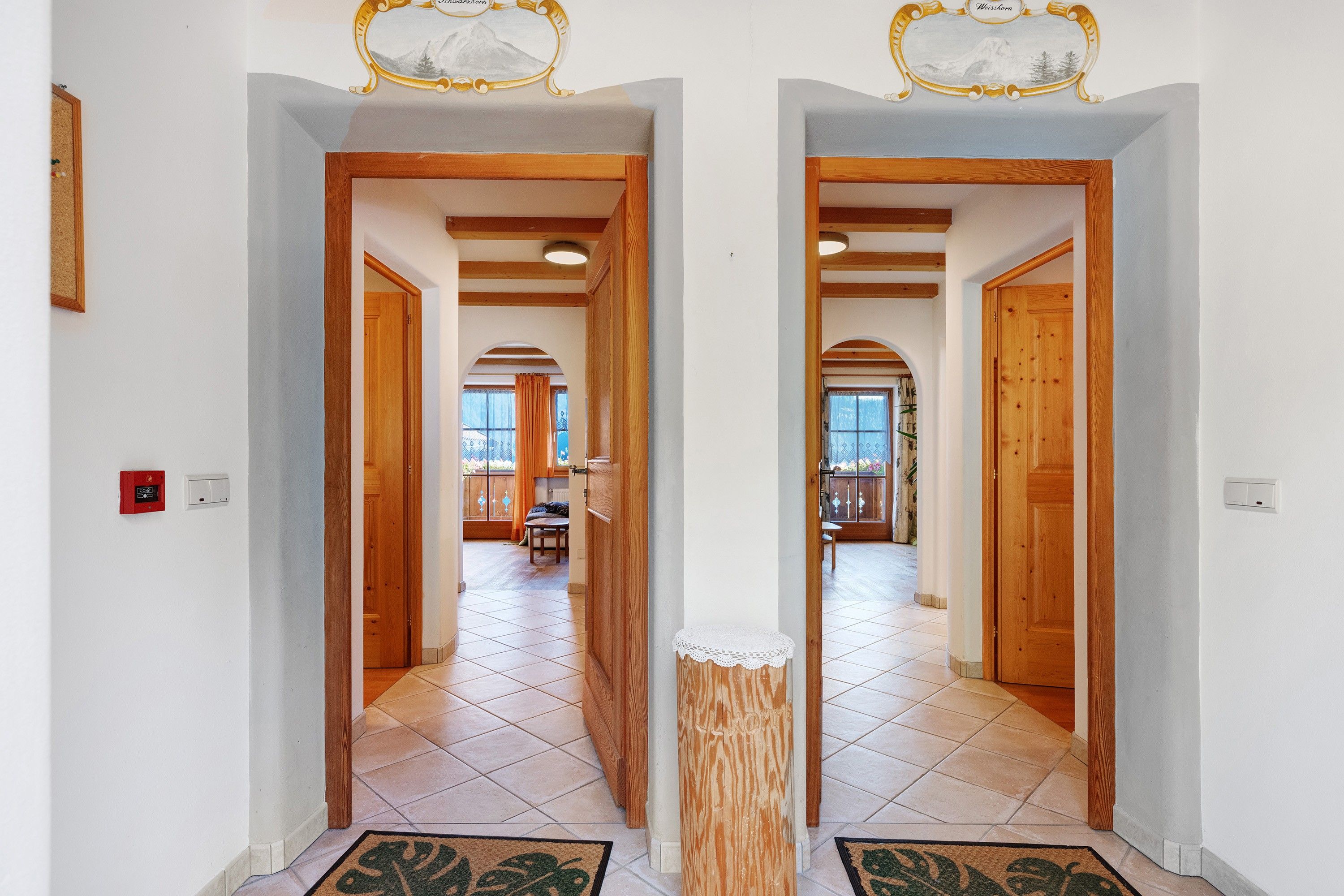 A hallway with wooden doors and a tiled floor leading to a dining area with a table and chairs.