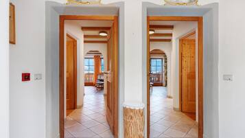 A hallway with wooden doors and a tiled floor leading to a dining area with a table and chairs.