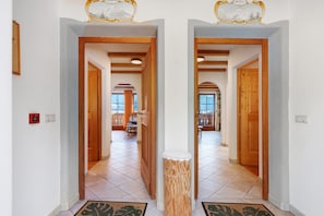 Un pasillo con puertas de madera y suelo de baldosas que conduce a un comedor con mesa y sillas.