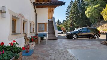 Un bâtiment doté d’une façade en bois, d’un escalier menant à un deuxième étage et d’un espace de stationnement où se trouve une voiture.