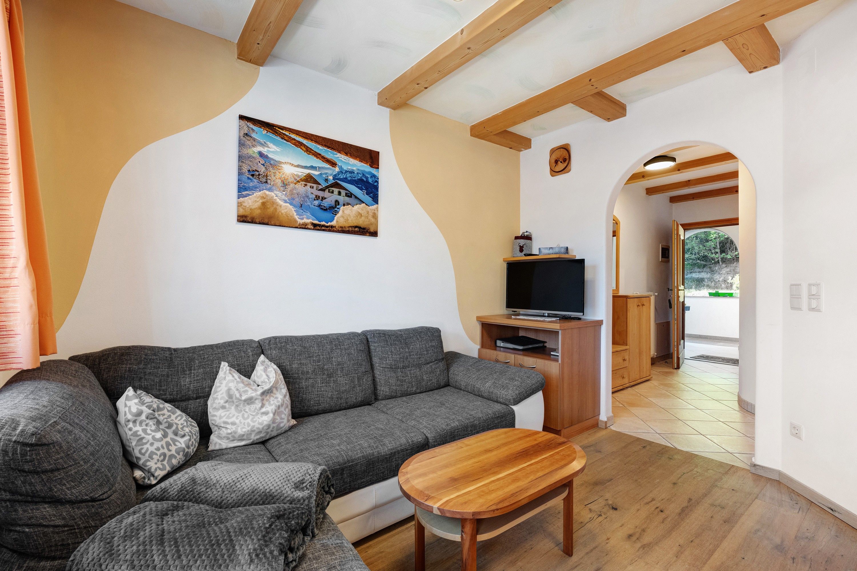 Una sala de estar con un sofá gris, una mesa de centro de madera, un cuadro en la pared y un mueble para televisor.